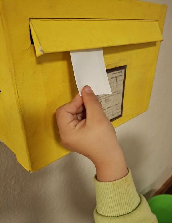 Briefkasten in den eine Kinderhand einen Brief einwirft