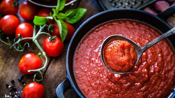 Tomaten auf Tisch und Kochtopf mit Schöpfkelle und Tomatensoße