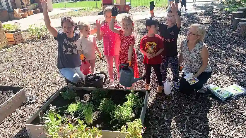 Zwei Erzieherinnen hocken mit einer Gruppen von Kindern vor einem Hochbeet