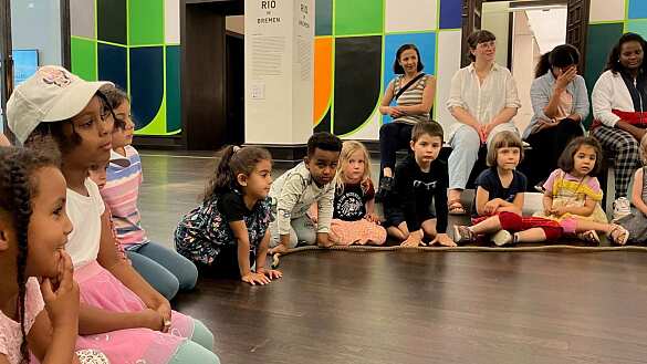 Kinder sitzen in der Kunsthalle auf dem Boden und hören gespannt zu. 