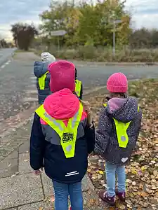 Kinder stehen an Straße mit Warnwesten. Aufnahme von hinten.