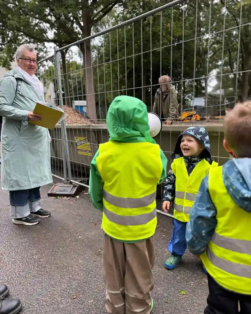 Baustellenbesuch: Elke Jungbluth vom Amt f&uuml;r soziale Dienste befragt gemeinsam mit Kindern die Bauarbeiter