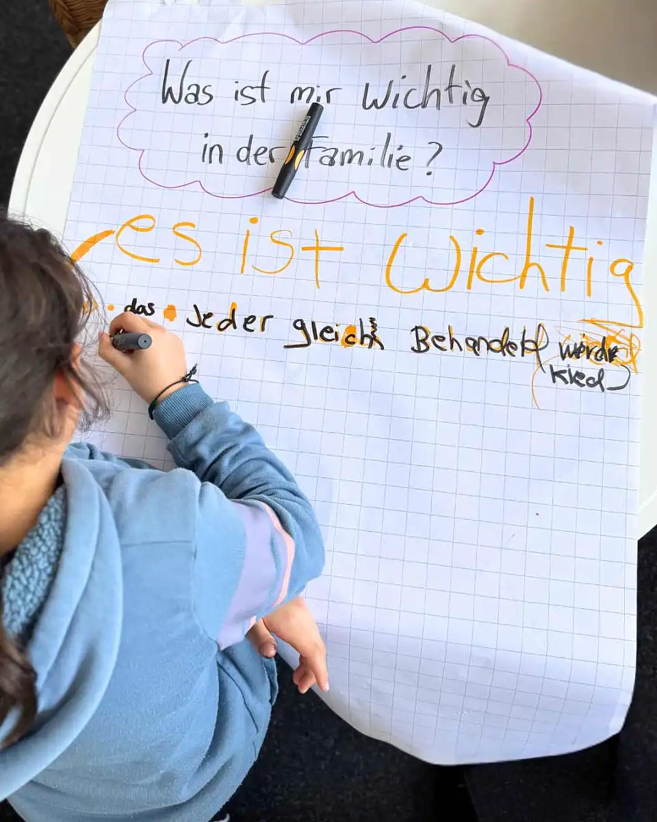 Kind schreibt auf Flipchart zur Fragestellung: Was ist mir wichtig in der Familie?