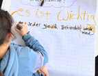 Kind schreibt auf Flipchart zur Fragestellung: Was ist mir wichtig in der Familie?