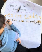 Kind schreibt auf Flipchart zur Fragestellung: Was ist mir wichtig in der Familie?