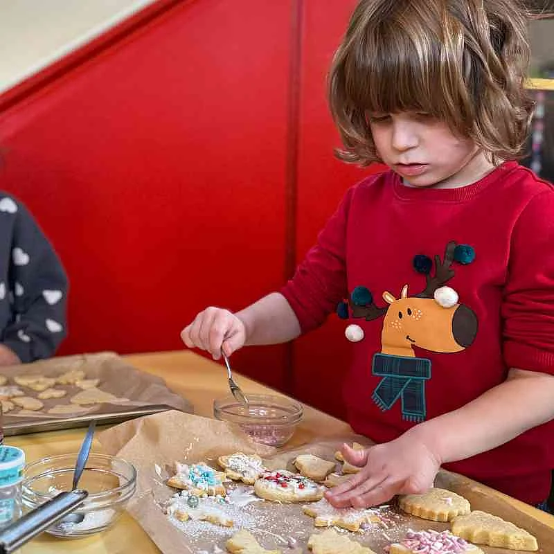 Ein Kind streut bunte Streusel auf Kekse