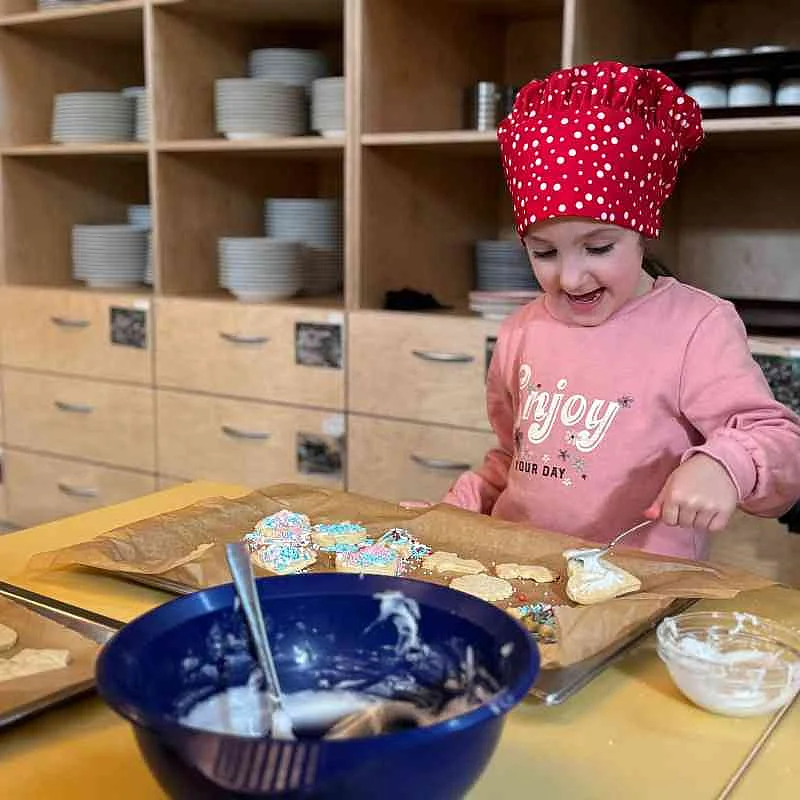 Ein Kind streut bunte Streusel auf Kekse