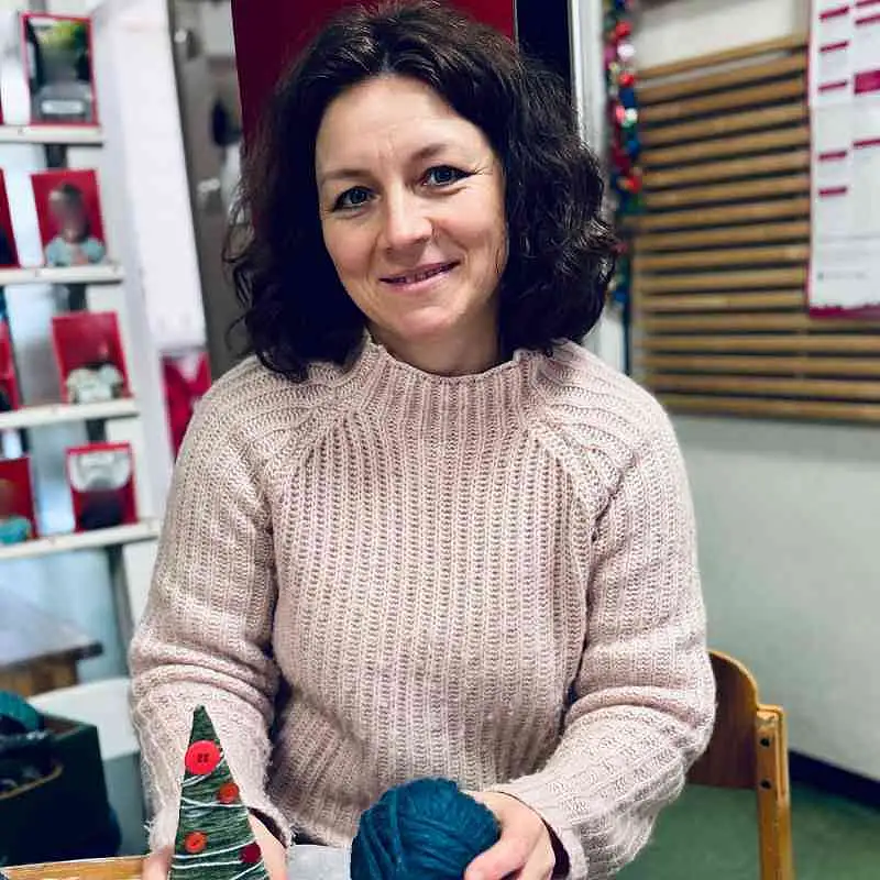 Fachkraft sitzt an einem Tisch und h&auml;lt einen gebastelten Tannenbaum und ein Wollkn&auml;ul in der Hand