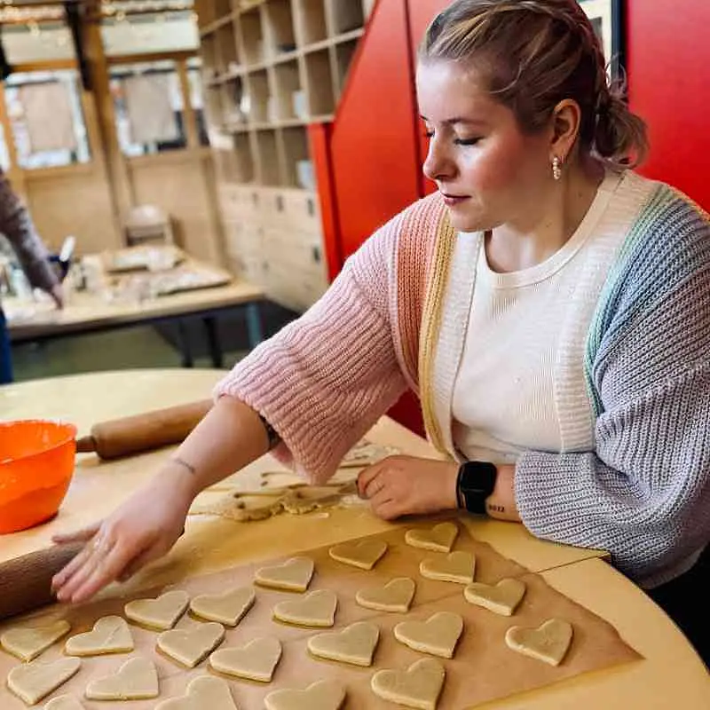 Fachkraft sitzt an einem Tisch und sticht Pl&auml;tzchen in Form eines Herzens aus einem Teig aus.