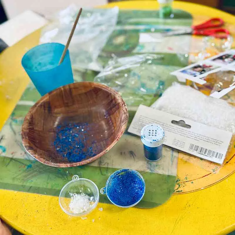 Glitzer und Tannenbaumkugeln liegen auf einem gelben Tisch