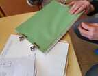 Ein Buch wird hergestellt: Papierstapel und eine Hand die mit Nadel und Faden den Rücken des Buches näht. 
