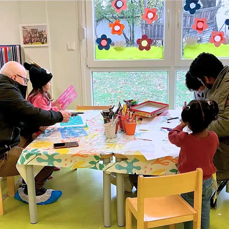 Zwei Väter sitzen mit ihren Kindern am Tisch und malen