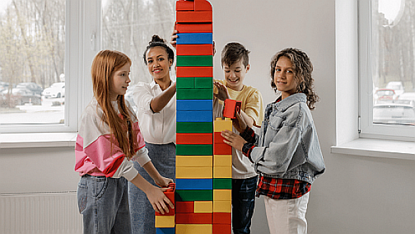 Kinder und Erzieherin bauen Turm aus Stapelsteinen