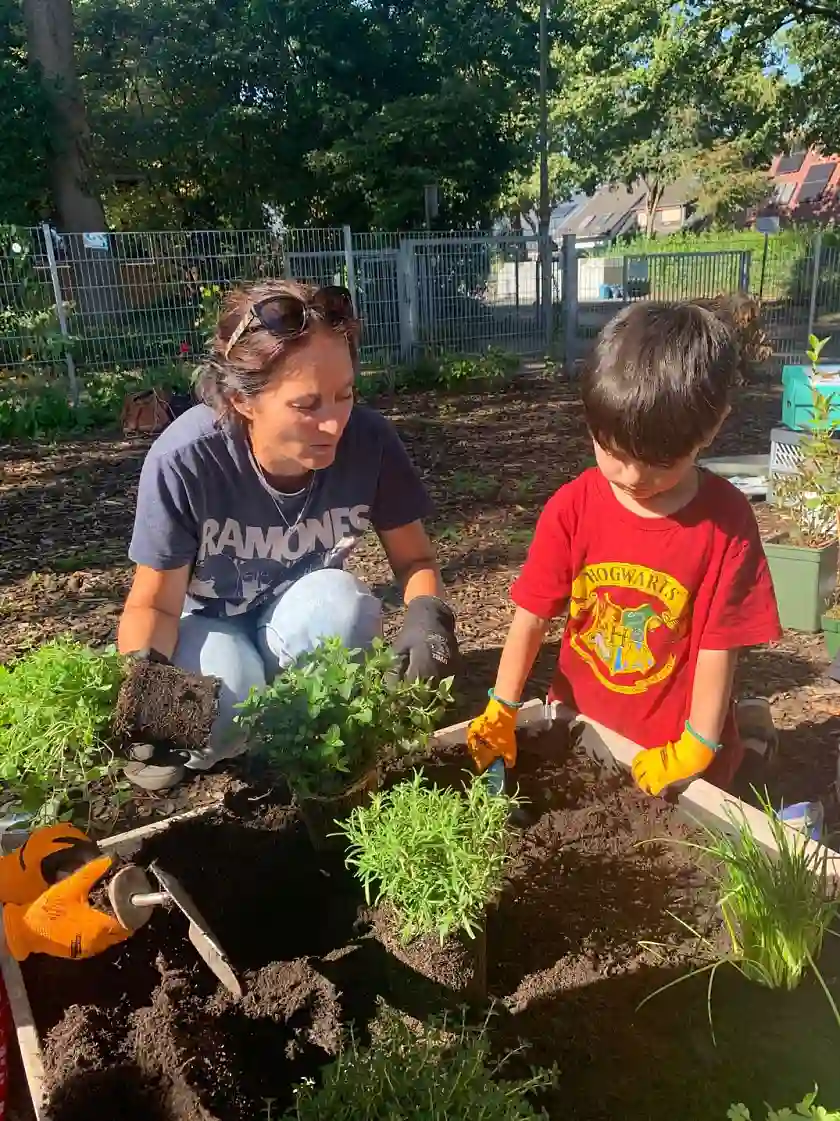 Eine Erzieherin und ein Kind bepflanzen ein Hochbeet