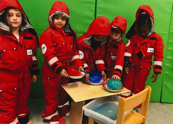 Kinder experimentieren mit Eis in roten Expeditionsanzügen