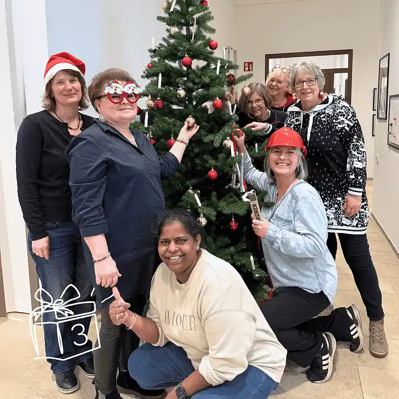 Kolleginnen der Infrastrukturdienste stehen um einen geschmückten Tannenbaum in der KiTa Bremen Zentrale