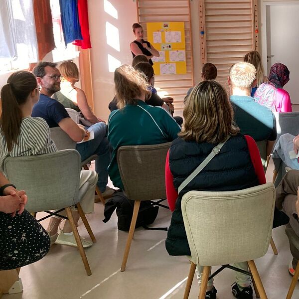 Eltern sitzen auf Stühlen; von hinten fotografiert