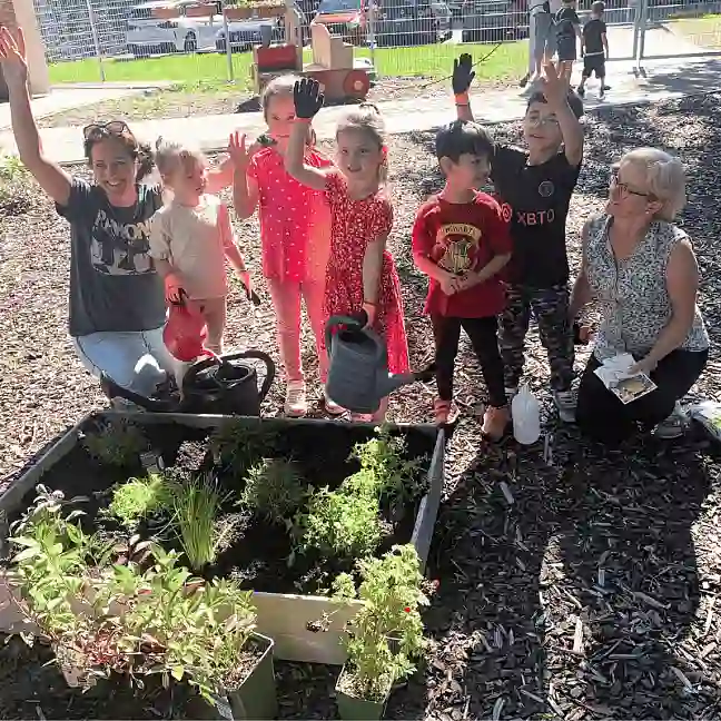 Zwei Erzieherinnen und eine Gruppe von Kindern stehen hinter einem neuen Hochbeet