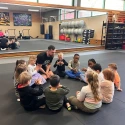 Kinder sitzen gemeinsam mit ihrem Trainer im Kreis in der Turnhalle