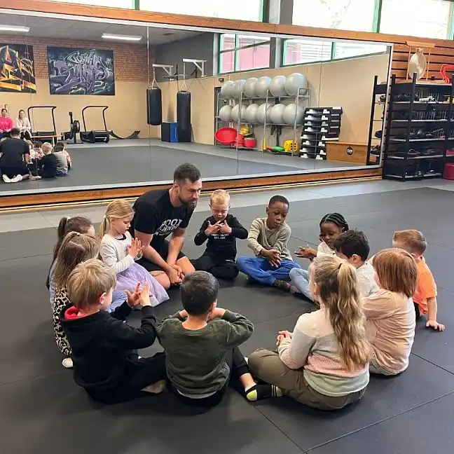 Kinder sitzen gemeinsam mit ihrem Trainer im Kreis in der Turnhalle