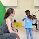 Frau hockt neben einem Geige spielendem Kind