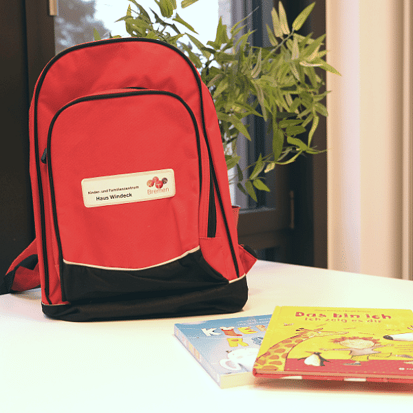 Roter Bücherrucksack auf Tisch mit zwei Büchern