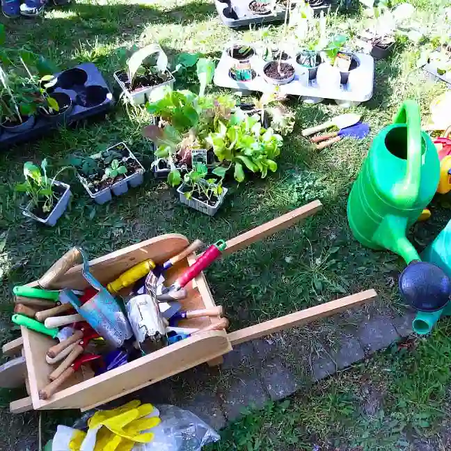 Holzschubkarre mit Gartengeräten und Gießkannen, die drumherum stehen